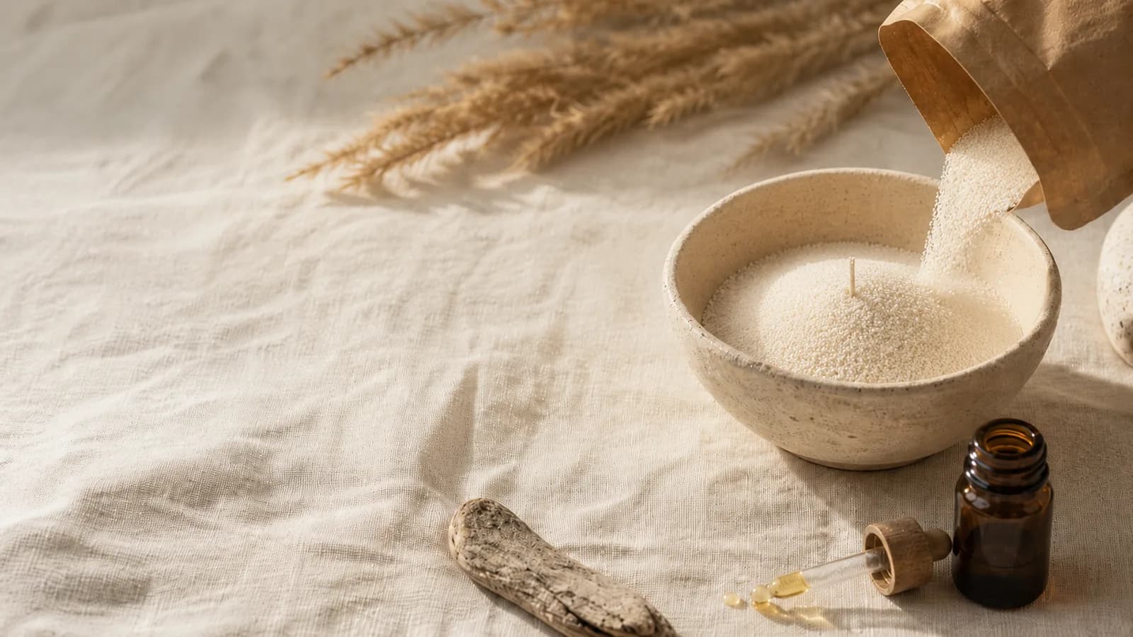 Sable de bougie versé dans une coupe en céramique, à côté d'un flacon de fragrance